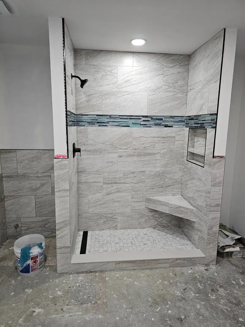 Porcelain marble-look shower walls with mosaic marble tile base, sandstone curb, and inset detailing