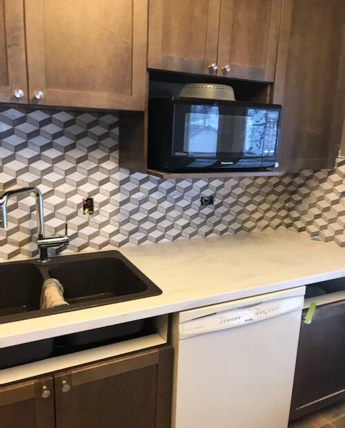 Mosaic tiles installed as backsplash in a kitchen with black and white pattern