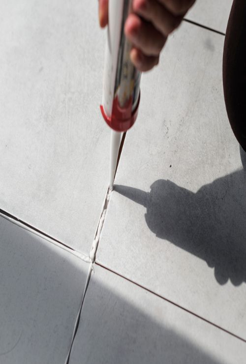 applying caulcking over re-grouted line on white tiles